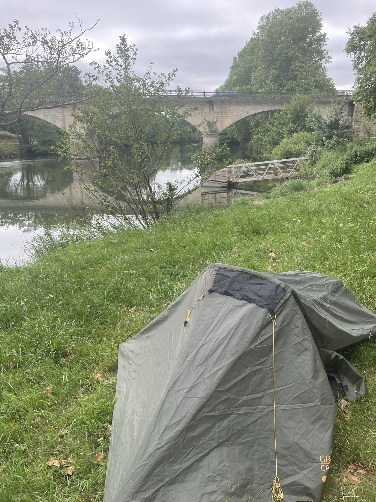 A small tent pitched on grass by a river