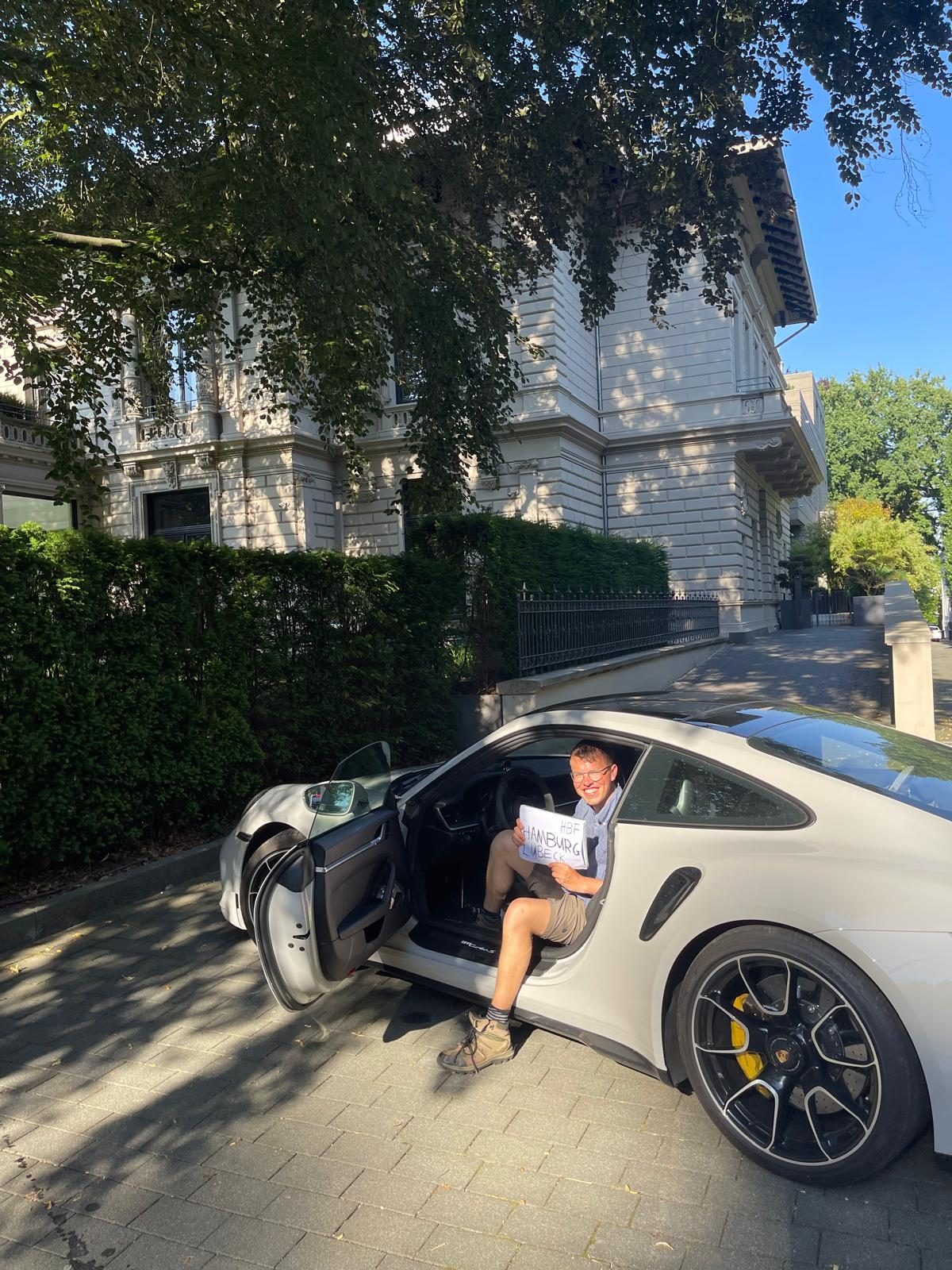 Johannes sitting in a white Porsche 911 outside a house in Hamburg